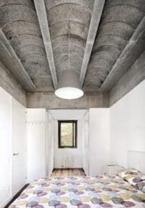 Dormitori modern Casa Ullastrell amb sostre volta de formigó vist i llit de disseny.