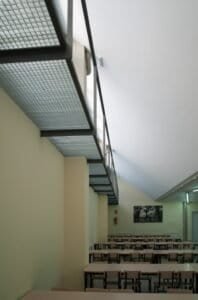 Interior menjador Carmelites amb sostre inclinat i detall constructiu de reixa metàl·lica.