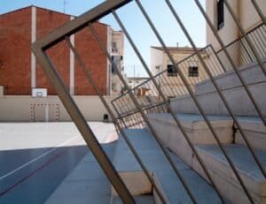 Pati exterior d'escola amb escales de formigó, baranes metàl·liques i façana de maó.