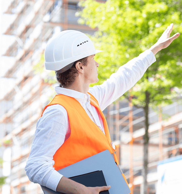 Tècnic d’obra amb casc i armilla reflectant inspeccionant una rehabilitació d’edifici a peu d’obra.